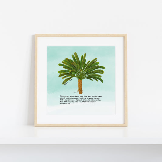 A framed art print featuring a watercolor-style green palm tree on a light aqua background, with a short poem printed below. The print is displayed in a light natural wood frame against a clean white wall.