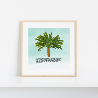 A framed art print featuring a watercolor-style green palm tree on a light aqua background, with a short poem printed below. The print is displayed in a light natural wood frame against a clean white wall.